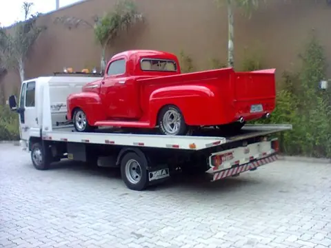 Guincho plataforma transportando picape antiga vermelha